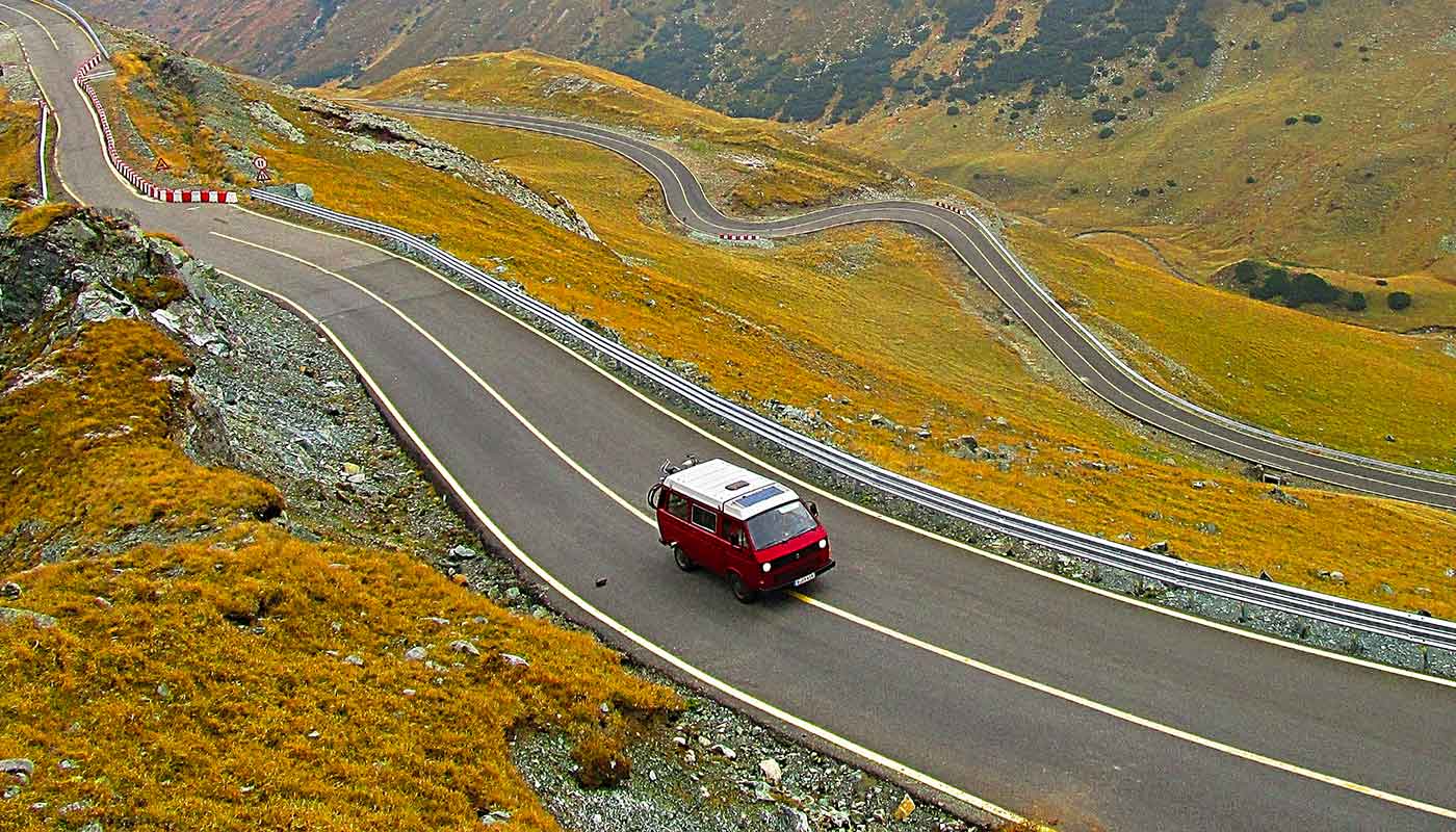 Un Van rouge roule sur une route de montagne